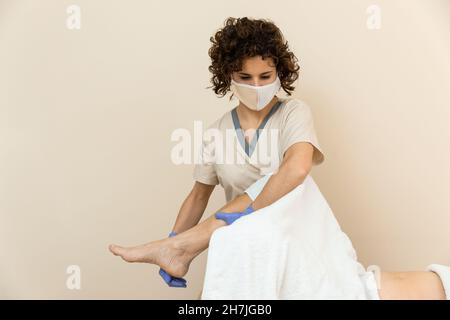 Physiotherapeut führt eine Beinmassage mit Handtüchern an die reife Frau durch Stockfoto