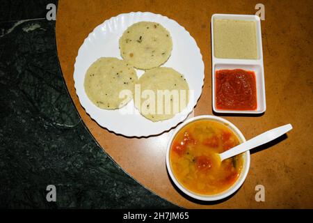 Beliebtes südindisches Frühstück Rava idli mit hausgemachtem Sambar und zwei Arten von Chutney, weißem Chutney und Rot auf dem Tisch serviert Stockfoto