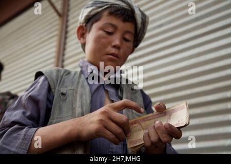 Ein kleiner Junge zählt sein Einkommen als Träger auf dem Hauptmarkt von Mazar-e-Sharif, in der nördlichen Provinz Balkh. Schätzungsweise 60.000 Kinder haben Stockfoto