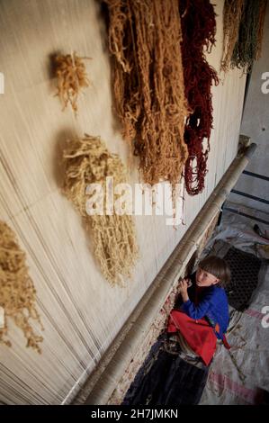 Aqila, 8, webt einen Teppich auf einem traditionellen Webstuhl, in ihrem Haus, im Dorf Ragshad, in der zentralen Provinz Bamyan. Ihr Vater arbeitet als Dail Stockfoto