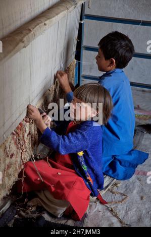 Aqila, 8, webt mit ihrem Bruder auf einem traditionellen Webstuhl einen Teppich in ihrem Haus, im Dorf Ragshad in der zentralen Provinz Bamyan. Her fath Stockfoto