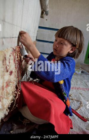 Aqila, 8, webt einen Teppich auf einem traditionellen Webstuhl, in ihrem Haus, im Dorf Ragshad, in der zentralen Provinz Bamyan. Ihr Vater arbeitet als Dail Stockfoto