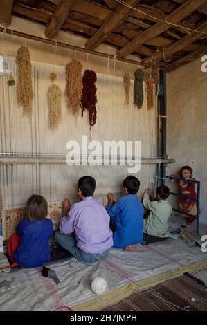 Ganz links - Aqila, 8, und ihre Brüder, die auf einem traditionellen Webstuhl einen Teppich weben, in ihrem Haus, im Dorf Ragshad, in der zentralen Bamyan-Provinz Stockfoto