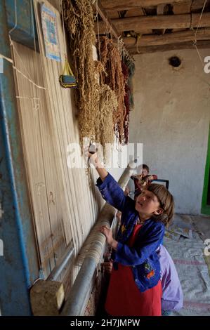 Ganz links - Aqila, 8, und ihre Brüder, die auf einem traditionellen Webstuhl einen Teppich weben, in ihrem Haus, im Dorf Ragshad, in der zentralen Bamyan-Provinz Stockfoto