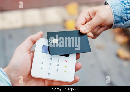 Von oben auf der Ernte gesichtslosen Client mit schwarzer Kreditkarte, während die Zahlung für den Kauf über NFC-Terminal auf der Straße Stockfoto
