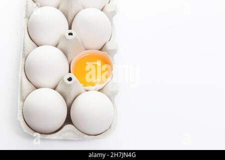 Auf dem weißen Hintergrund sind sechs Hühnereier in einem grauen Pappbehälter isoliert. Ein Ei ist gebrochen. Speicherplatz kopieren. Für Text platzieren Stockfoto