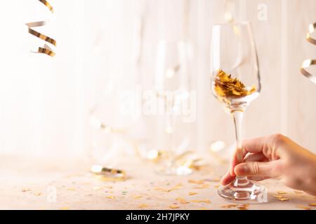 Die Champagner-Gläser des neuen Jahres in der Hand mit funkelnden Innenräumen. Auf weißem Hintergrund aus Lametta und Bändern. Vorderansicht. Stockfoto