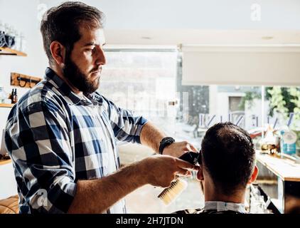 Friseur schneidet die Haare des Kunden. Prozess des Trimmens in der Frisierwerkstatt. Stockfoto