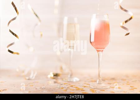 Neujahrsgläser mit rosa-weißem Champagner auf weißem Hintergrund mit Glitzer und Lametta. Vorderansicht. Stockfoto