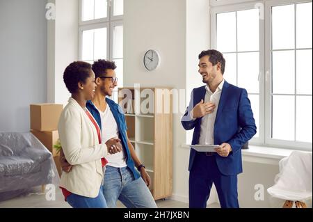 Glückliches afroamerikanisches Paar, das über lustigen Witz beim Treffen mit makler lacht, der ihnen Haus zeigt. Stockfoto