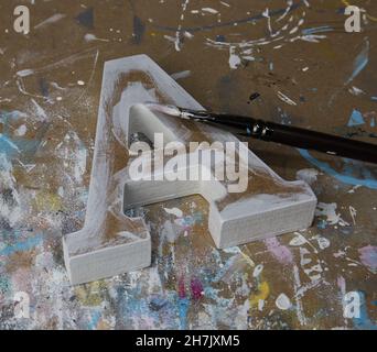 Unfertiger und teilweise bemalter Brief A aus MDF auf einem Werkstatttisch mit Pinsel Stockfoto