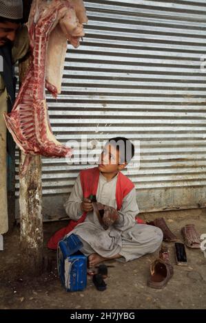 Auf dem Hauptmarkt von Mazar-e-Sharif in der nördlichen Provinz Balkh arbeitet ein Schuhputzer, der neben einer Metzgerei sitzt. Schätzungsweise 60.000 Stockfoto