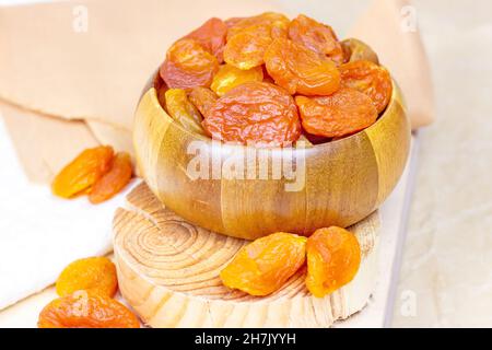Orangefarbene getrocknete Aprikosen in Holzschüssel auf hellem Hintergrund. Stockfoto