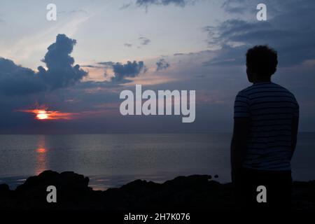 Landschaftsfoto eines Mannes oder einer Person, die das Meer oder Meer bei Sonnenuntergang oder Sonnenaufgang beobachtet Stockfoto