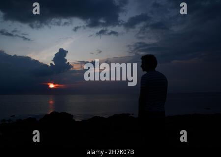 Landschaftsfoto eines Mannes oder einer Person, die das Meer oder Meer bei Sonnenuntergang oder Sonnenaufgang beobachtet Stockfoto