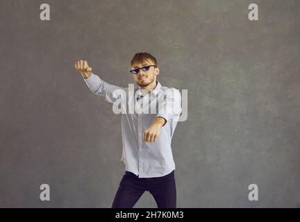 Glücklicher junger Mann in einer zerlumpen Lebensbrille, der gangnam-Stil auf grauem Hintergrund tanzt Stockfoto