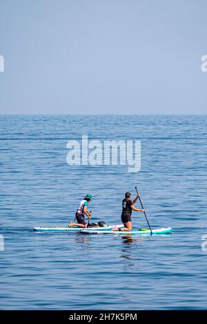 Paddelboarder auf einem ruhigen Meer vor Megavissey, Cornwall, Großbritannien. Stockfoto