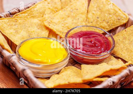 Gelb salzig knackig und knusprig Dreieck mexikanischen Mais Nachos mit Sauce in einer Schüssel auf hellem Holzhintergrund. Stockfoto