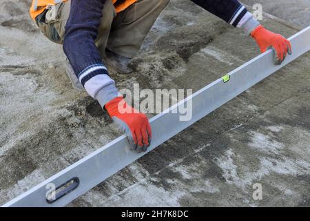 Nahansicht eines Arbeiters, der ein ebenes Werkzeug in der Nivelliervorbereitung auf einer sandigen Basis die Pflastersteine hält Stockfoto