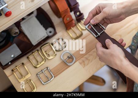 Nahaufnahme Hände von professionellen Gerber Wahl Gürtelschnalle auf Holztisch in Leder-Werkstatt Stockfoto