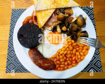 Englisches Bauernhaus Frühstück mit gut gemachten Speck Spiegelei Würstchen gebackene Bohnen Pilze und schwarzen Pudding mit weißen gebutterten Toast Stockfoto