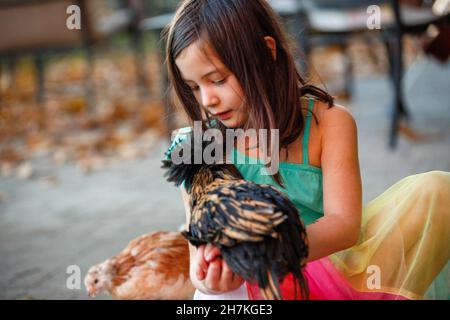 Nahaufnahme eines glücklichen kleinen Mädchens, das draußen mit Hühnern sitzt Stockfoto