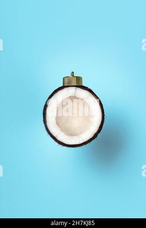 weihnachtskugeldekoration aus Kokosnuss auf blauem Hintergrund mit Schatten. Minimales Neujahrskonzept. Nahaufnahme Stockfoto