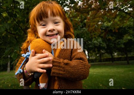 Lächelndes Mädchen mit Down-Syndrom umarmen Spielzeug im Park Stockfoto