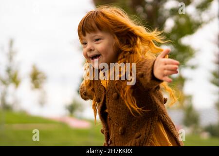 Fröhliches Mädchen mit Down-Syndrom läuft im Park Stockfoto