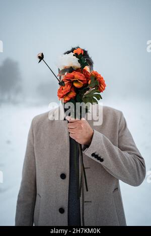 Mann bedeckt Gesicht mit Blumenstrauß im Winter Stockfoto