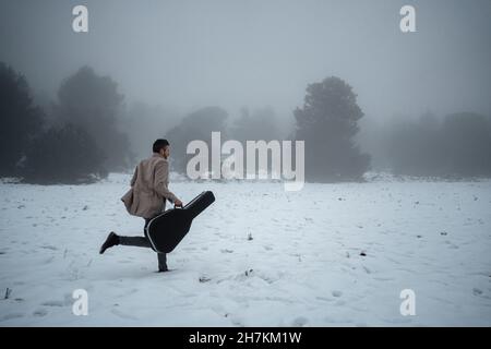 Reifer Mann mit Gitarrenkoffer, der im Winter auf Schnee läuft Stockfoto