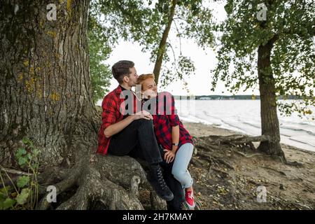Mann, der Frau küsst, während er unter dem Baum sitzt Stockfoto