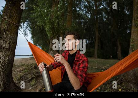 Mann mit Thermoskanne sitzt in der Hängematte Stockfoto