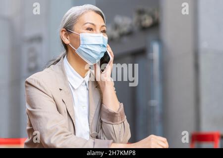 Frau trägt eine schützende Gesichtsmaske und spricht auf dem Smartphone Stockfoto