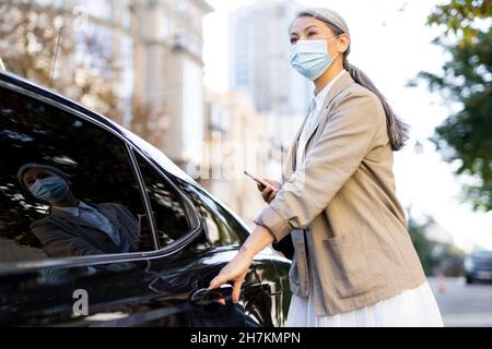 Frau trägt eine schützende Gesichtsmaske, die die Tür des Taxis öffnet Stockfoto