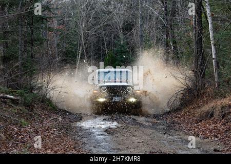 Ein Jeep-Wrangler, der durch eine gefrorene Schlammpfütze fährt und Wasser und Eis auf einer Forststraße in den Adirondack Mountains, NY, durch die Luft schickt Stockfoto