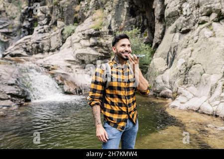 Lächelnder Mann mit mittlerem Erwachsenen, der Rucksack trägt und am Teich im Wald steht Stockfoto