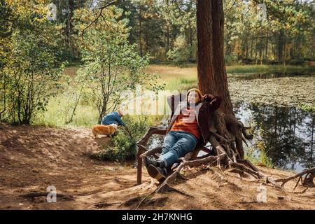 Mann mit Händen hinter dem Kopf, der sich am Baum im Wald entspannt Stockfoto