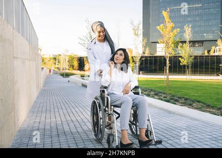 Junge Allgemeinpraktikerin mit der Hand eines Patienten, der im Rollstuhl sitzt Stockfoto