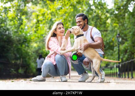 Glückliches junges Paar, das im öffentlichen Park mit Hund spielt Stockfoto