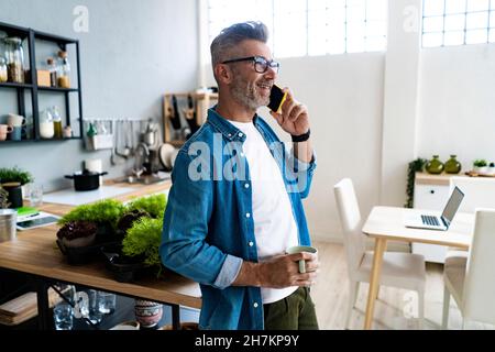 Mann hält die Kaffeetasse, während er zu Hause auf dem Mobiltelefon spricht Stockfoto