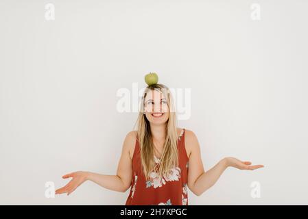 Glückliche Frau balanciert Apfel auf dem Kopf vor der Wand Stockfoto