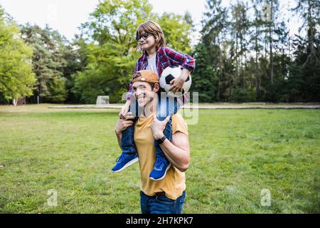 Lächelnder Vater, der Sohn auf den Schultern im Park trägt Stockfoto