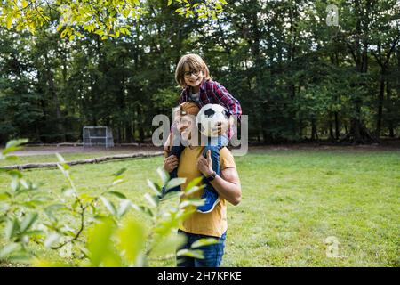 Lächelnder Mann, der seinen Sohn auf den Schultern im Park trägt Stockfoto