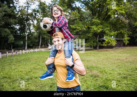 Fröhlicher Vater trägt Sohn hält Fußball im Park Stockfoto