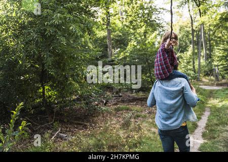 Junge mit Stock, der im Wald auf den Schultern des Mannes sitzt Stockfoto