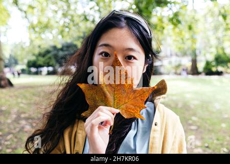 Frau, die im Park den Mund mit Ahornblatt bedeckt Stockfoto