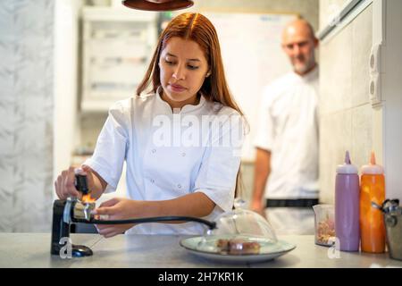 Weibliche Köchin verwendet Rauchmelder beim Kochen in der Küche Stockfoto