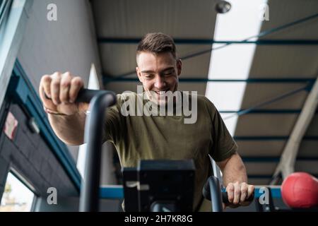 Lächelnder männlicher Athlet, der im Fitnessstudio auf einem Crosstrainer trainiert Stockfoto