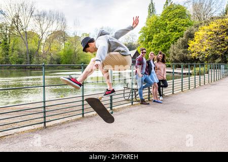 Junger Mann zeigt seinen Freunden im Park Stunt auf dem Skateboard Stockfoto